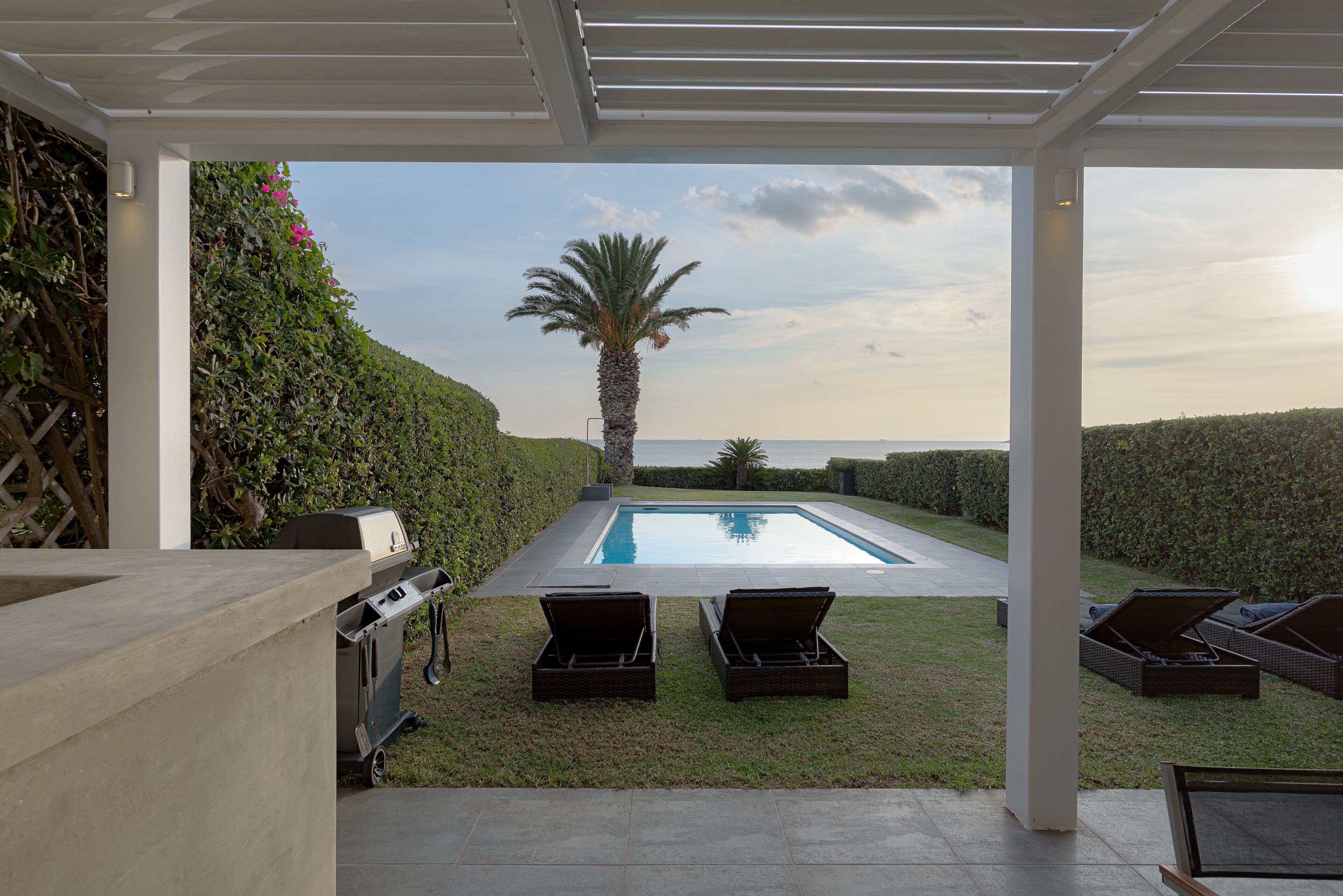A covered outdoor area with a pool, lounge chairs, and a grill.