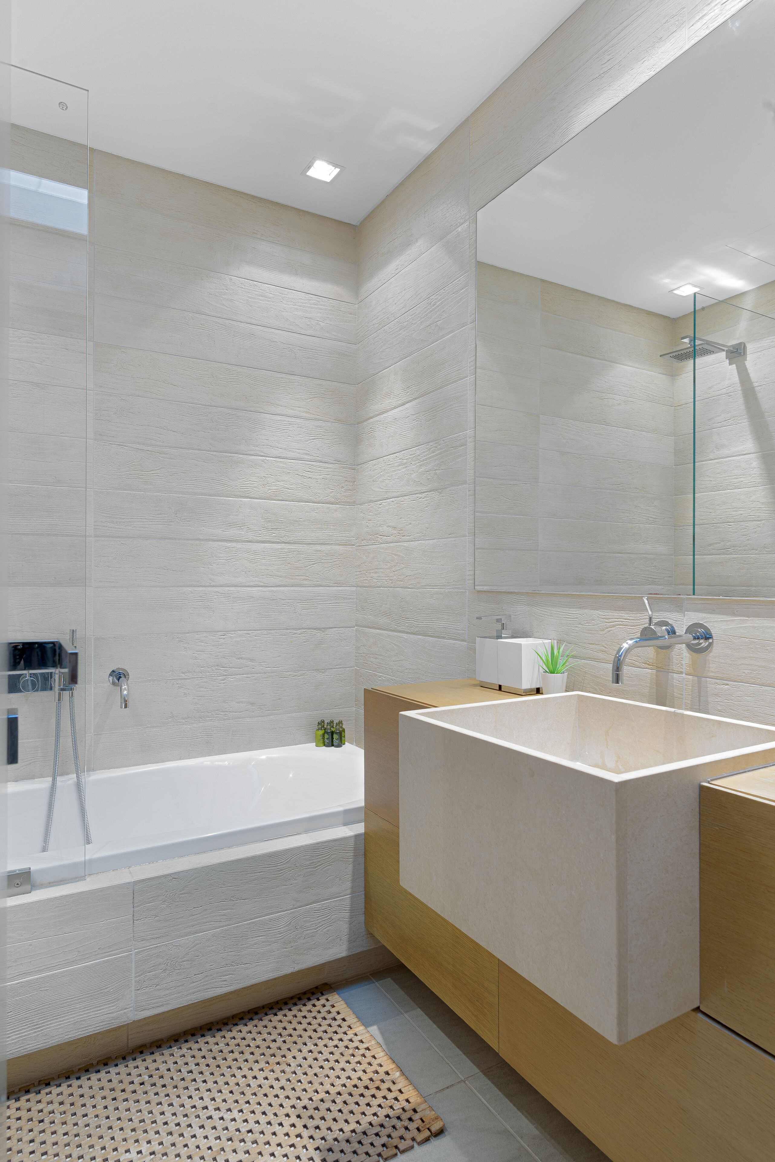 A modern bathroom with a large bathtub, a glass shower enclosure, and a wooden vanity with a mirror.