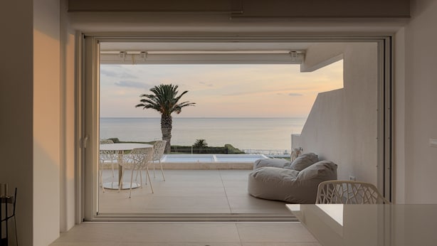 Ein modernes Zimmer mit einer großen Schiebeglasdoor, die auf einen Balkon mit Meerblick und einer Palme führt.