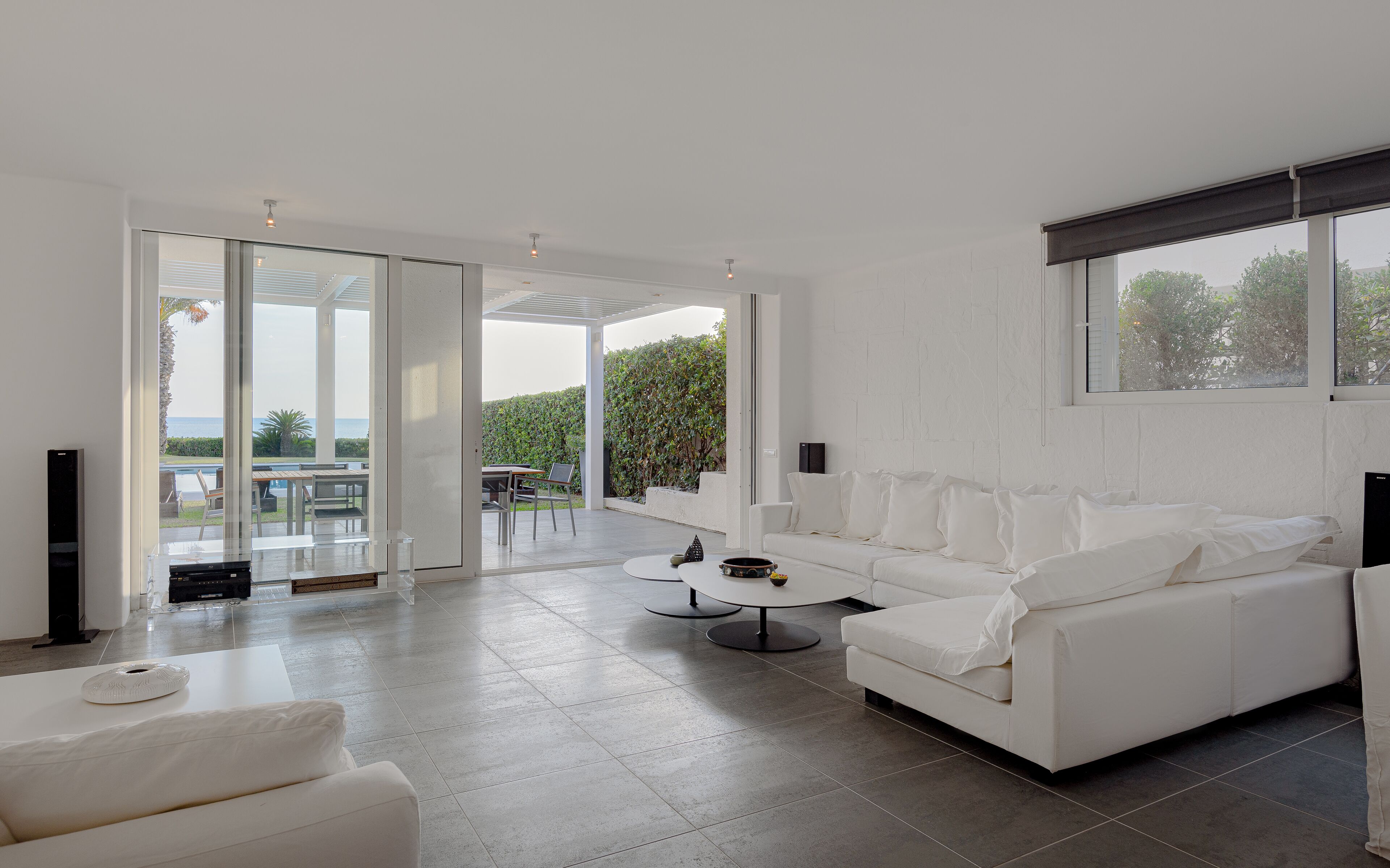 Ein geräumiger Wohnbereich mit einem weißen Sofa, einem Couchtisch und einem Fernseher. Eine Glastür öffnet sich zu einer Terrasse mit Blick auf das Meer.