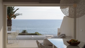 Ein Balkon mit Meerblick, weiße Stühle, ein Tisch und eine Obstschale.