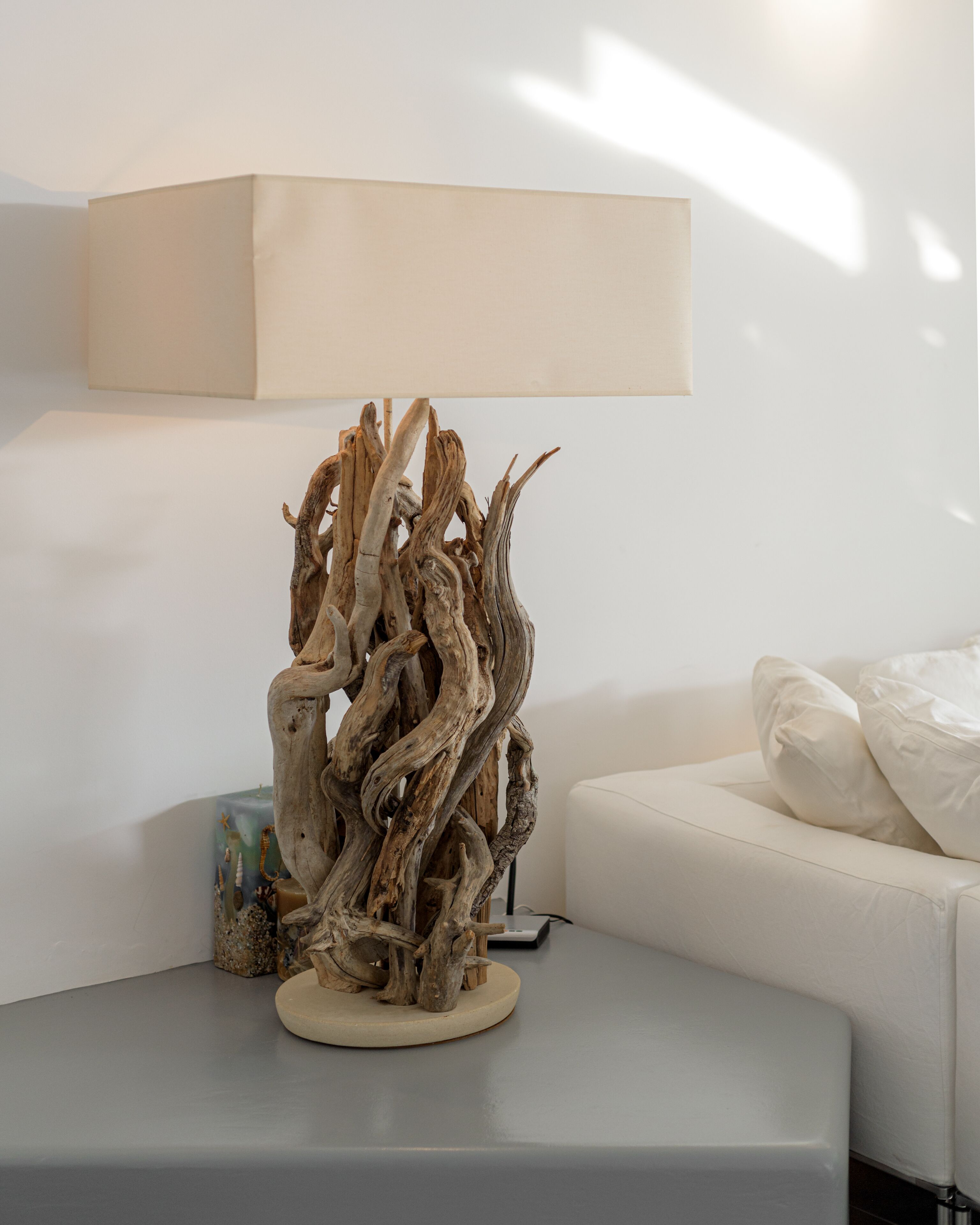 Een moderne woonkamer met een witte bank, een houten sculptuur op een tafel en een lamp met een beige lampenkap.