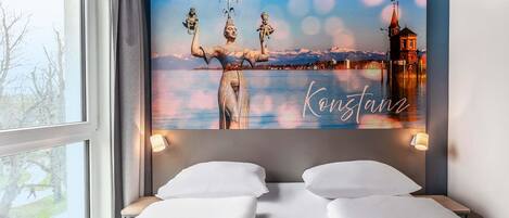 Habitación de hotel con una cama, un mural grande en la pared y una ventana con vistas a árboles.
