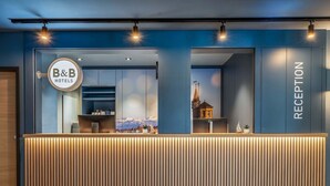 A hotel reception desk with a 'B&B Hotels' sign, a reception area, and a view of a church. - B&B Hotel Konstanz (Konstanz)