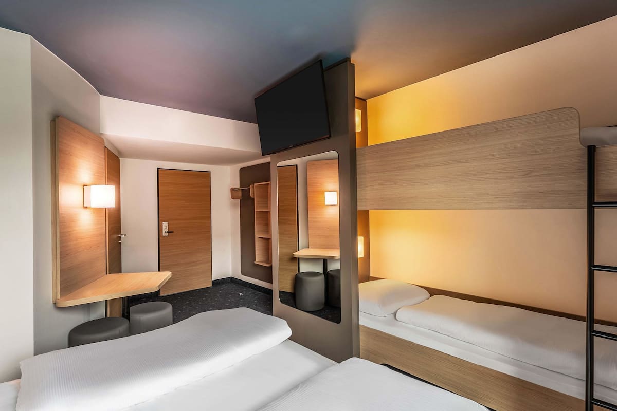 A hotel room with bunk beds, a flat-screen TV, a wooden wardrobe, and a small seating area.