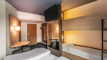 A hotel room with bunk beds, a flat-screen TV, a wooden wardrobe, and a small seating area.