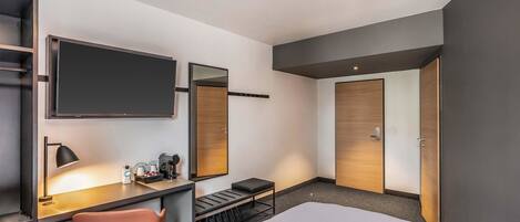 Una habitación de hotel con cama, escritorio con silla, televisión, espejo y puerta.