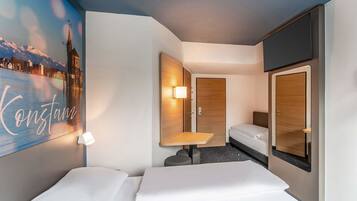 Ein Hotelzimmer mit Bett, Schreibtisch, Stuhl, Spiegel und einem an der Wand befestigten Fernseher.