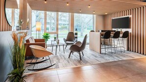 A modern interior with a wooden slatted ceiling, a flat-screen TV, a bar area, and seating arrangements. - B&B Hotel Konstanz (Konstanz)