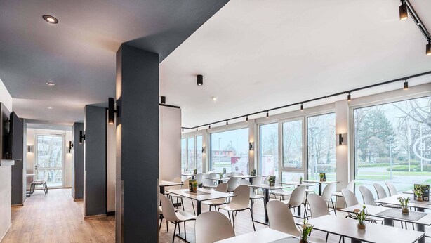 A modern dining area with tables and chairs, large windows, and a view of the outside. - B&B Hotel Konstanz (Konstanz)