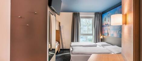 Una habitación de hotel con cama, escritorio, televisor y ventana con cortinas.