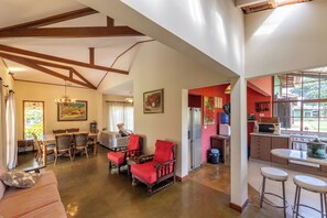 A spacious living area with a dining table, red chairs, a sofa, and a kitchen with a stove and microwave.
