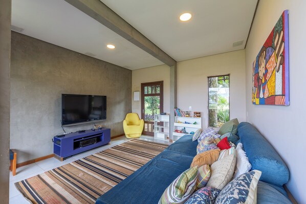 A modern living room with a flat-screen TV, a blue sofa, a yellow chair, and a colorful painting on the wall.