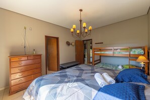 A bedroom with a bed, a dresser, a chandelier, and a door leading to another room.
