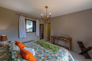 A bedroom with a bed, a bedside lamp, a wooden nightstand, a mirror, and a window with curtains.