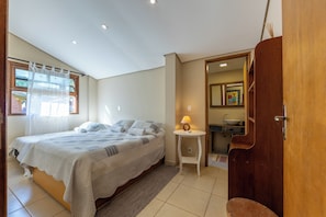 A bedroom with a bed, a bedside table with a lamp, a bathroom with a sink and mirror, and a wooden door. - Stables 90 minutes from São Paulo (Cesário Lange)