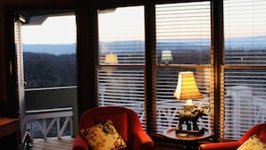 A room with two red armchairs, a small table with a lamp, and large windows offering a view of the outdoors. - One of the Best Views in Wintergreen! (Wintergreen Resort)