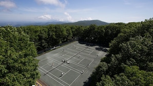 A tennis court surrounded by dense trees, with a clear sky and distant mountains. - One of the Best Views in Wintergreen! (Wintergreen Resort)