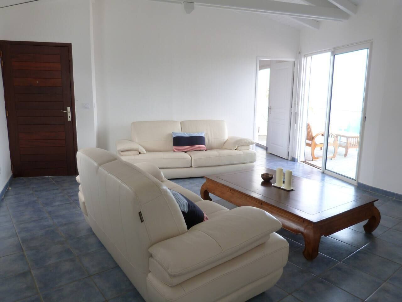A spacious living room with a large sofa set, a wooden coffee table, and a sliding glass door leading to an outdoor area.