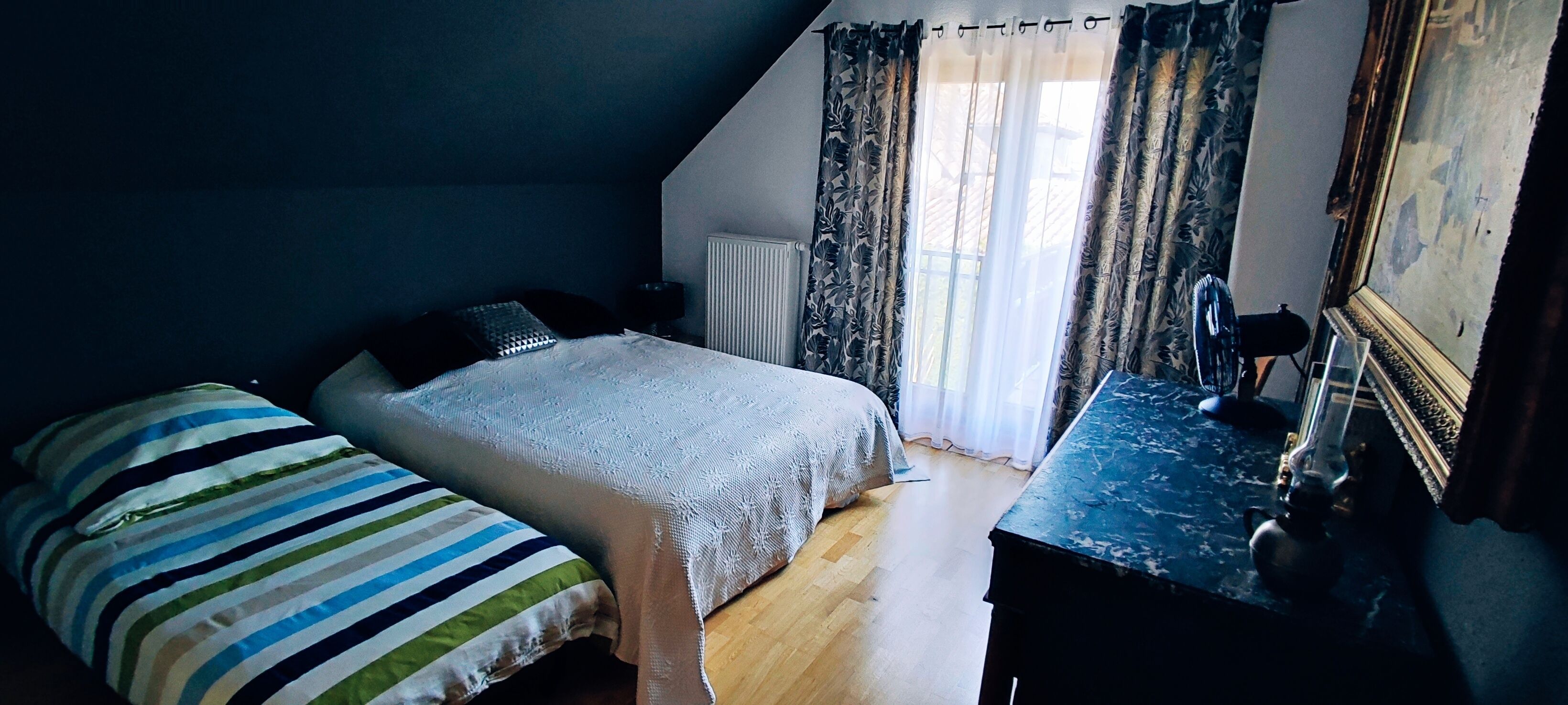 A bedroom with a bed, a dresser, a radiator, and a window with curtains.