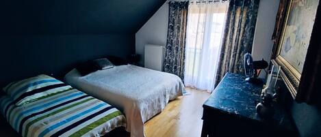 A bedroom with a bed, a dresser, a radiator, and a window with curtains.