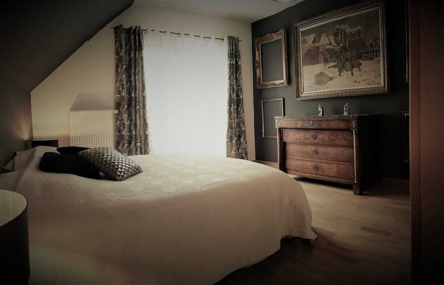 A bedroom with a large bed, a dresser, and a painting on the wall.