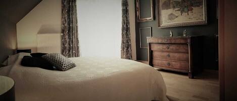 A bedroom with a large bed, a dresser, and a painting on the wall.