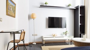 A modern hotel room with a flat-screen TV, a desk with a chair, a bedside table with a lamp, and a bed. - Where you Want to be! Acogedor Piso en el Centro (Málaga)