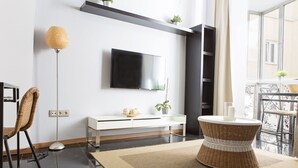 A modern living room with a flat-screen TV, a white console table, a wicker chair, a floor lamp, and a round wicker coffee table. - Where you Want to be! Acogedor Piso en el Centro (Málaga)