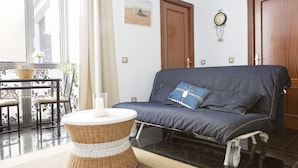 A living room with a sofa, a round wicker table, a clock on the wall, and a door. - Where you Want to be! Acogedor Piso en el Centro (Málaga)