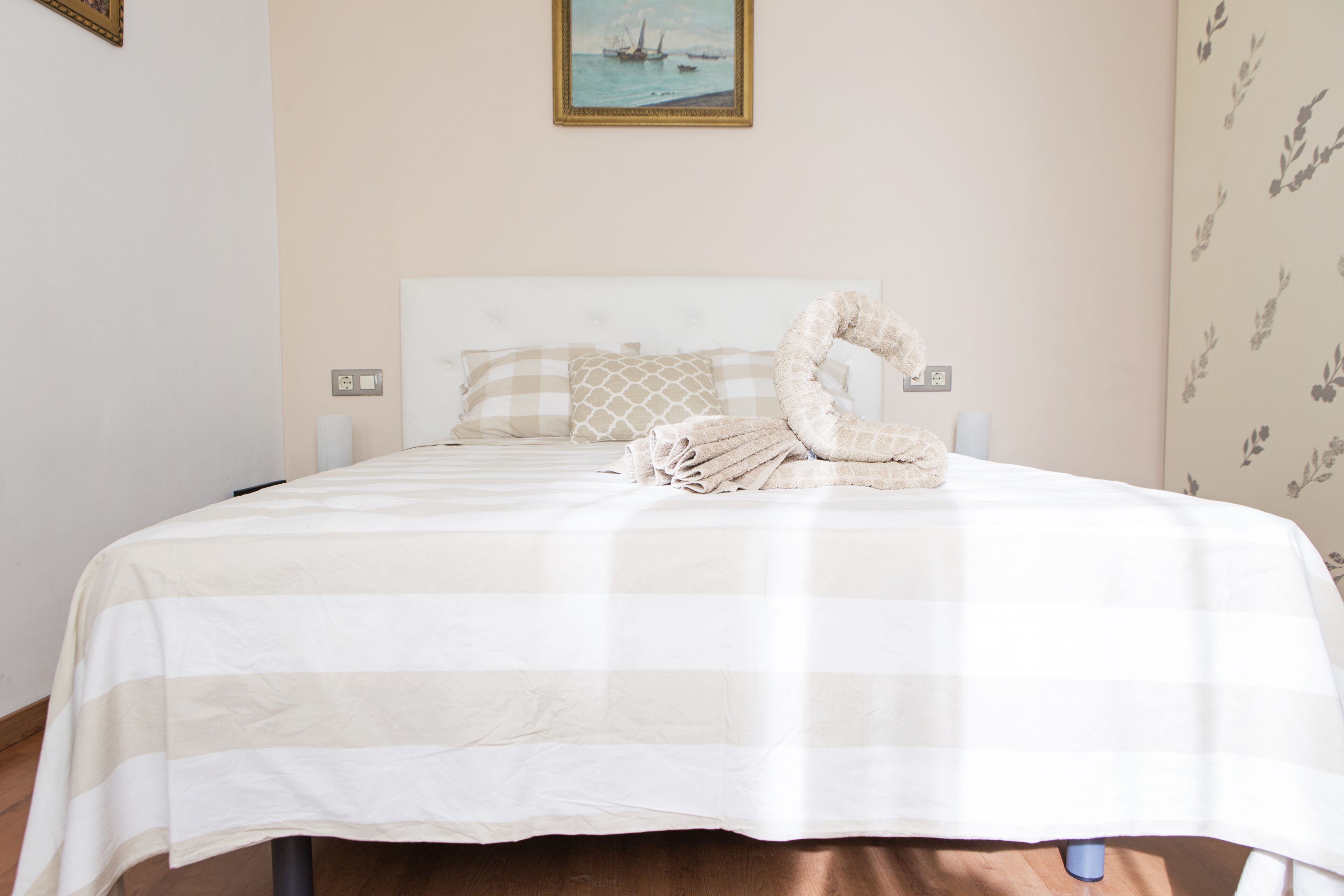 A neatly made bed with a striped bedspread, a pillow with a geometric pattern, and a towel arranged in a swan shape.