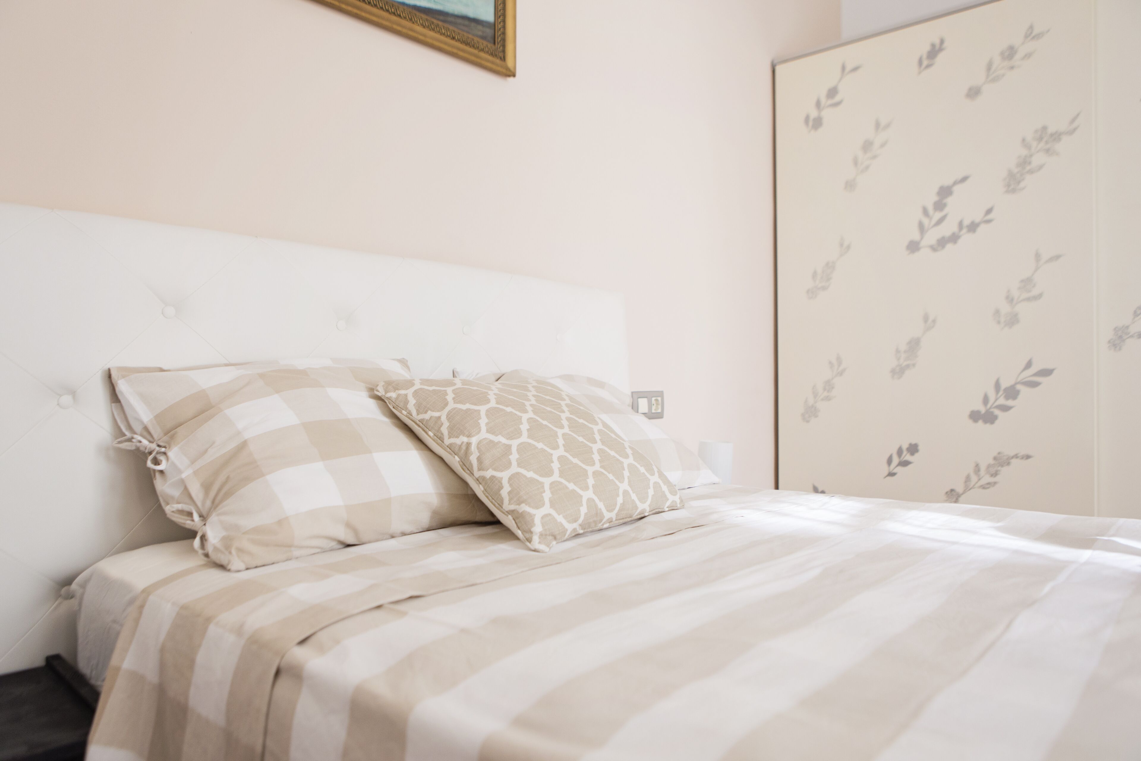A neatly made bed with striped bedding and two pillows, a white headboard, and a wall with a floral pattern.