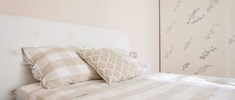 A neatly made bed with striped bedding and two pillows, a white headboard, and a wall with a floral pattern.