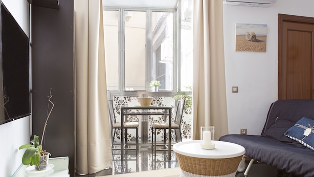 A modern living room with a sofa, a round wicker table, and a TV mounted on the wall. - Where you Want to be! Acogedor Piso en el Centro (Málaga)