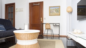 A modern living room with a round wicker coffee table, a sofa, a desk with a chair, and a flat-screen TV mounted on the wall. - Where you Want to be! Acogedor Piso en el Centro (Málaga)