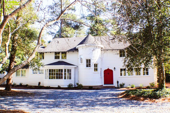 A white two-story house with a red door and multiple windows.