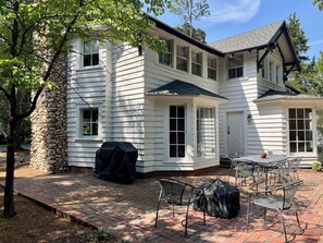 A two-story house with a stone foundation, a covered patio with metal chairs, and a brick pathway.