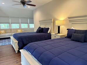 A bedroom with two beds, a sofa, a ceiling fan, and a window with blinds.