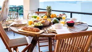 Une table de petit-déjeuner avec des fruits, du pain et des boissons, placée sur un balcon offrant une vue panoramique.