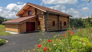 Una cabaña de troncos con techo de tejas rojas, un porche de madera y una puerta roja.