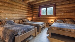 Un dormitorio de cabaña de troncos con dos camas de madera, una ventana con cortina y una lámpara en el techo.