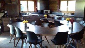 Una cocina moderna con armarios oscuros, un microondas y una estufa. Hay un comedor con una mesa grande y sillas, y un jarrón con flores amarillas sobre la mesa.