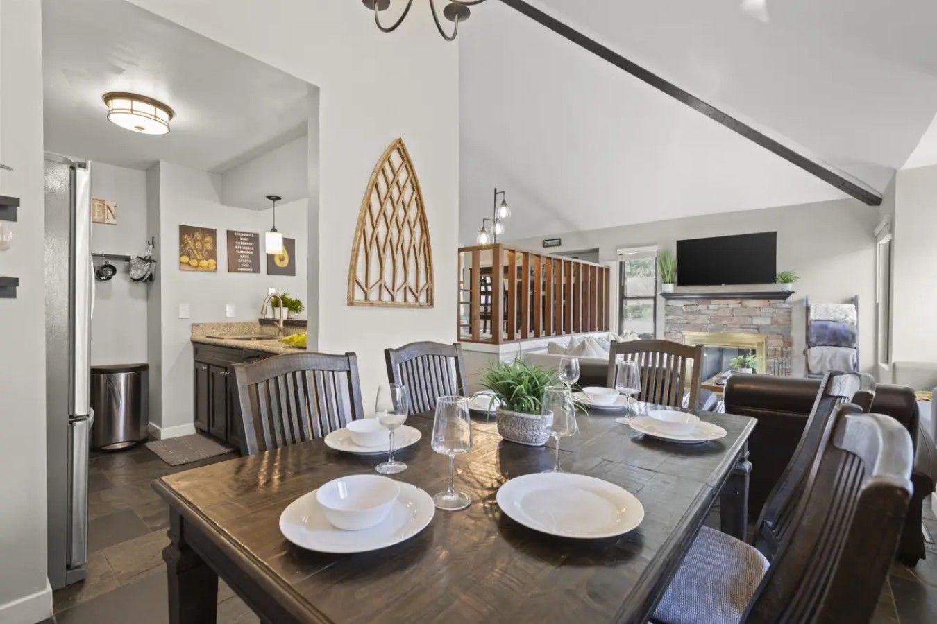 A dining area with a dark wooden table set for six, surrounded by chairs. A decorative wall piece is above the table.