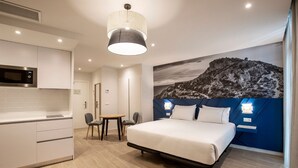 A modern hotel room with a bed, a dining table with chairs, a kitchenette, and a large wall mural. - Tandem Portal de Elche (Alicante)