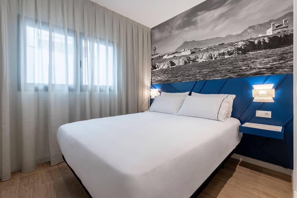 Een hotelkamer met een groot bed, uitzicht op een kustlandschap en een blauwe accentmuur.