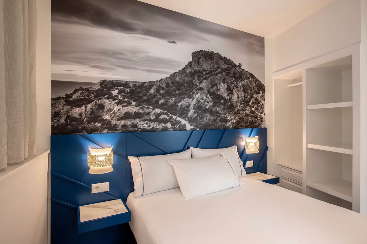 Een slaapkamer met een groot bed, een hoofdeinde met een berglandschap op de muur, nachtlampjes en een inbouwkast.