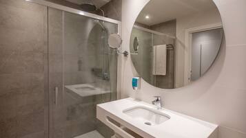 A modern bathroom with a glass-enclosed shower, a white sink, and a large mirror.
