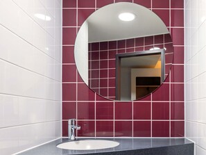 A bathroom with a round mirror, white sink, and red-tiled walls. - B&B Hotel Stuttgart-Bad Cannstatt (Stuttgart)