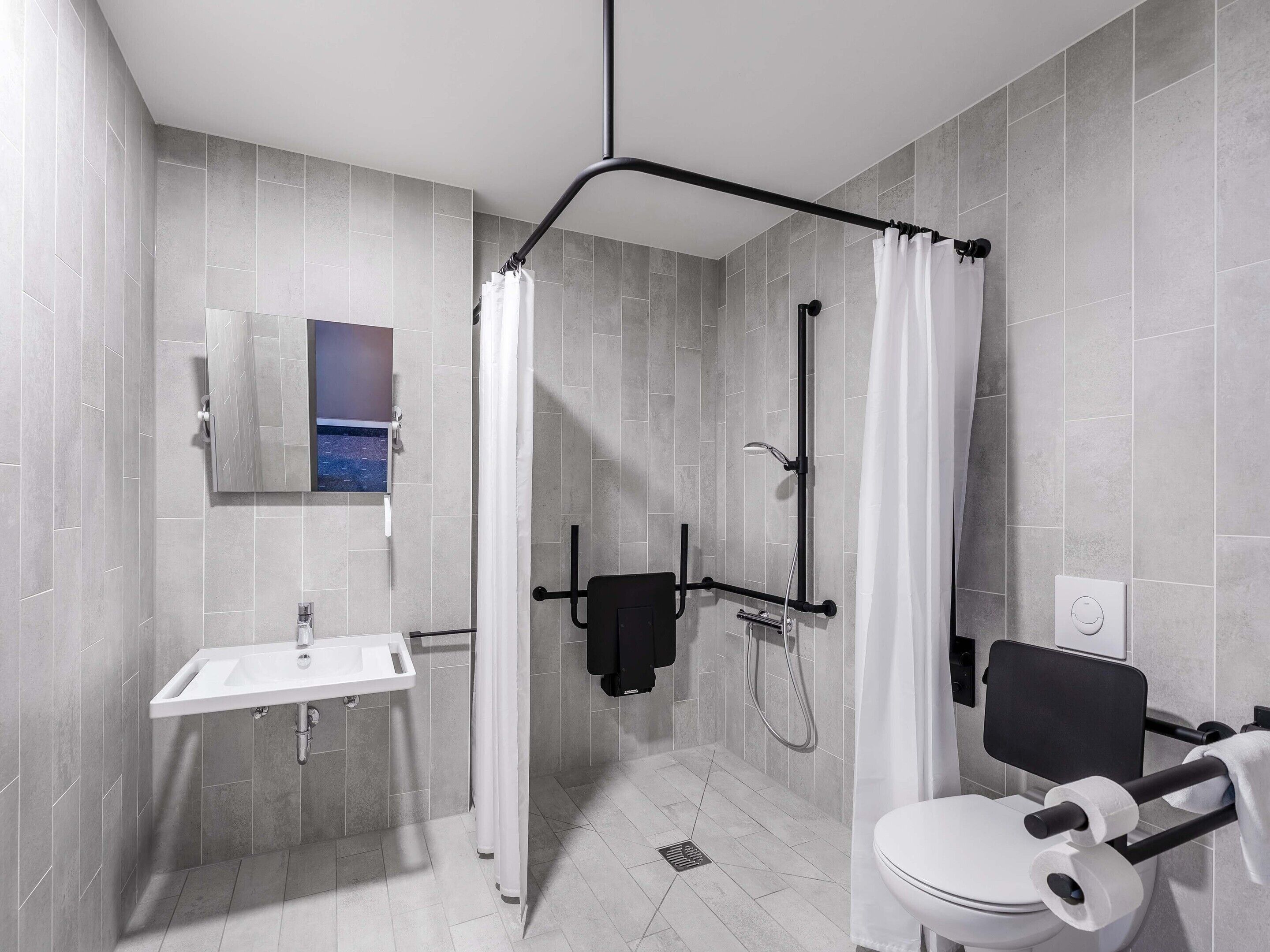 Une salle de bain moderne équipée d’une douche, de toilettes, d’un lavabo et d’un miroir fixé au mur.