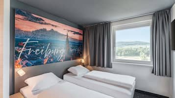 A hotel room with two beds, a large cityscape painting on the wall, a window with a view, and a lamp.